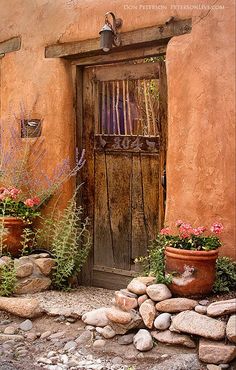 an old adobe building with potted plants and flowers in front of the entrance door