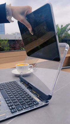 a person is holding an open laptop with their hand on the keyboard and coffee cup in front of them