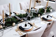 the table is set with black and white place settings, gold candlesticks, greenery and striped napkins