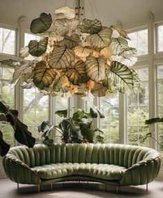 a green couch sitting under a chandelier in a living room next to large windows