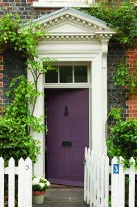 a white picket fence and red door in front of a brick building with ivy growing on it