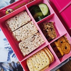 a pink lunch box with crackers, fruit and nuts in the middle on a table