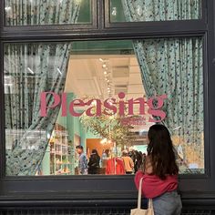 a woman standing in front of a store window with the words pleasing written on it