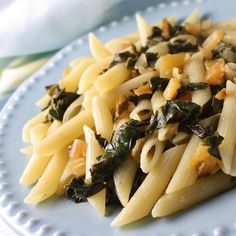 a white plate topped with pasta and spinach on top of a blue table cloth