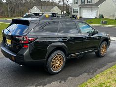 a black suv with gold rims parked on the side of the road in front of a house