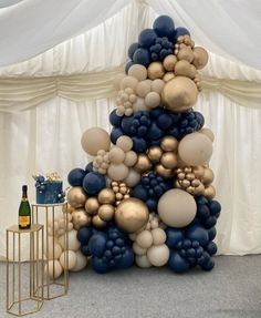 a large balloon christmas tree with gold and blue balloons on it's top, next to a bottle of champagne