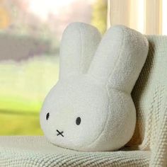 a white stuffed animal sitting on top of a couch next to a window sill