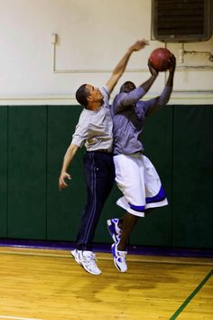 two men are playing basketball in an indoor court while one man jumps up to grab the ball