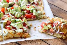 a pizza with avocado and tomatoes on it sitting on a piece of parchment paper