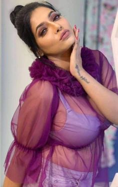 a woman with tattoos on her arm and purple dress posing in front of a mirror