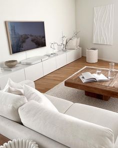 a living room filled with white furniture and a flat screen tv mounted on the wall