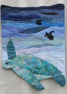a quilted wall hanging with a turtle on it's back and two birds flying over the water