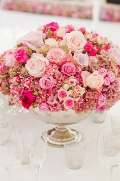 a vase filled with pink and white flowers on top of a table next to wine glasses