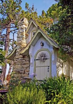 a small white house with a clock on it's front door in the woods