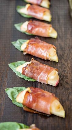 several pieces of bacon wrapped in leafy greens on a wooden table with other food items