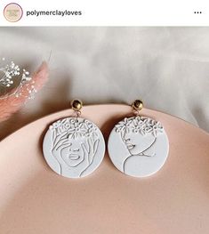 pair of white earrings with woman's face and flowers on the front, sitting on a pink plate