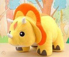 a stuffed animal that is yellow with orange ears and tail, standing in front of a tree