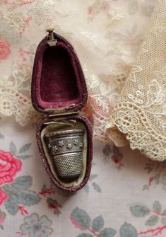 an open shoe box sitting on top of a lace covered table cloth next to a pink rose