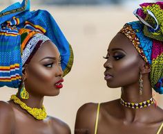 two african women wearing head wraps and necklaces, one is looking at the other