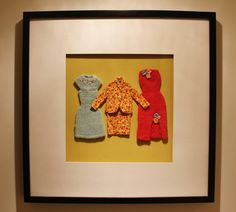 two baby clothes are hanging on the wall in front of a framed photo with yellow background