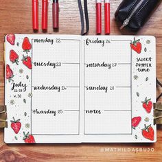 an open planner with strawberries on it next to two pens and a pencil case