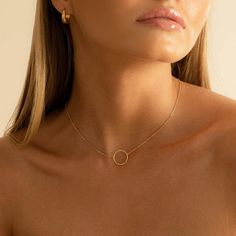 a woman wearing a gold necklace with a circle pendant on it's neck, looking off to the side