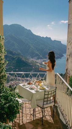 a woman sitting at a table on top of a balcony with a view of the ocean