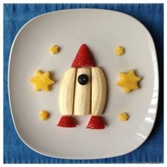 a white plate topped with cut up fruit shaped like a rocket ship on top of banana slices