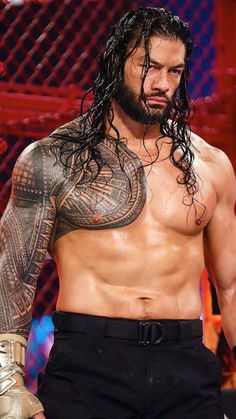 a man with long hair and tattoos standing in front of a wrestling ring holding a metal glove