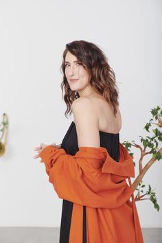 a woman in an orange and black dress is posing for the camera with her arms crossed