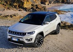 a white jeep parked on top of a sandy beach next to the ocean and rocks