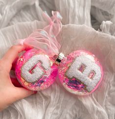 someone is holding two ornaments with the letters d and b on them in pink, white and gold