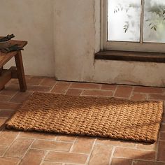 a door mat sitting on the floor in front of a window with a bench next to it