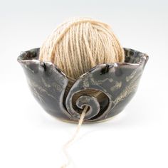 a ball of yarn sitting in a bowl on top of a white surface with a rope