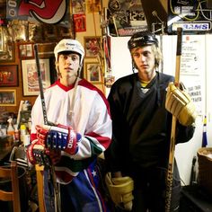 two young men standing next to each other in a room filled with hockey gear and memorabilia