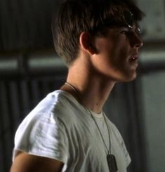 a young man wearing glasses and a white t - shirt looks off into the distance