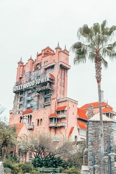 the hollywood tower hotel is pink and has a palm tree in front of it on a cloudy day