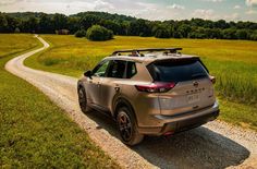 the rear end of a silver suv driving down a dirt road in a grassy field