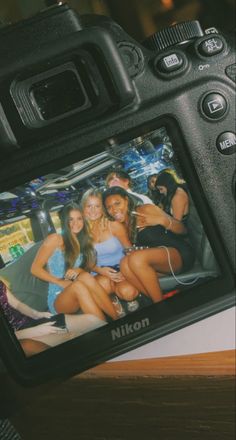 a digital camera sitting on top of a wooden table next to two beautiful young women