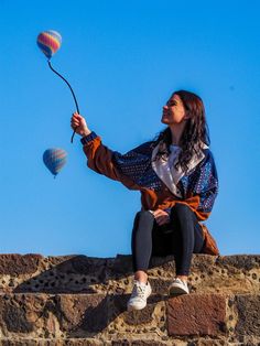 a woman sitting on top of a stone wall flying a hot air balloon