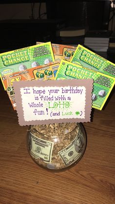 a glass jar filled with lots of money sitting on top of a wooden table next to a sign that reads, i hope your birthday is filled with a whole lotto