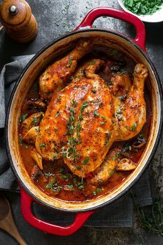 a red pot filled with chicken covered in sauce and garnished with parsley