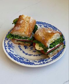 two sandwiches are sitting on a plate with blue and white trimmings, one is cut in half