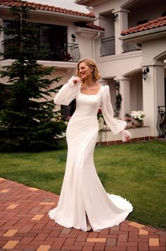 a woman in a white dress is posing for the camera on a brick walkway near some houses