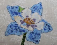 a blue and white flower with green leaves on it's center is embroidered onto fabric