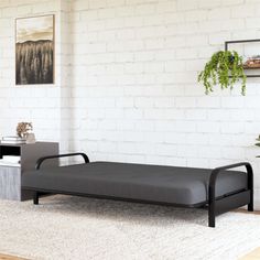 a black daybed sitting in front of a white brick wall and potted plant