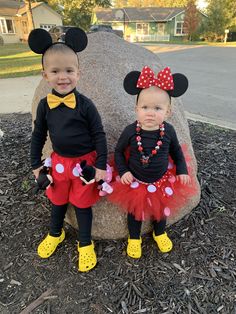 two young children dressed in mickey and minnie mouse costumes sitting next to each other on a rock
