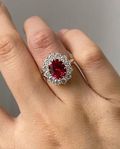 a woman's hand with a red and white diamond ring on top of it