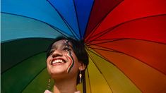 a woman with her face painted and holding an open rainbow umbrella in front of her