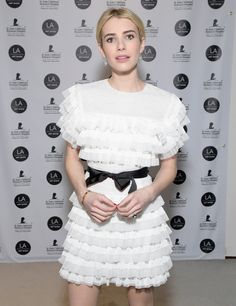 a woman standing in front of a wall wearing a white dress and black bow tie